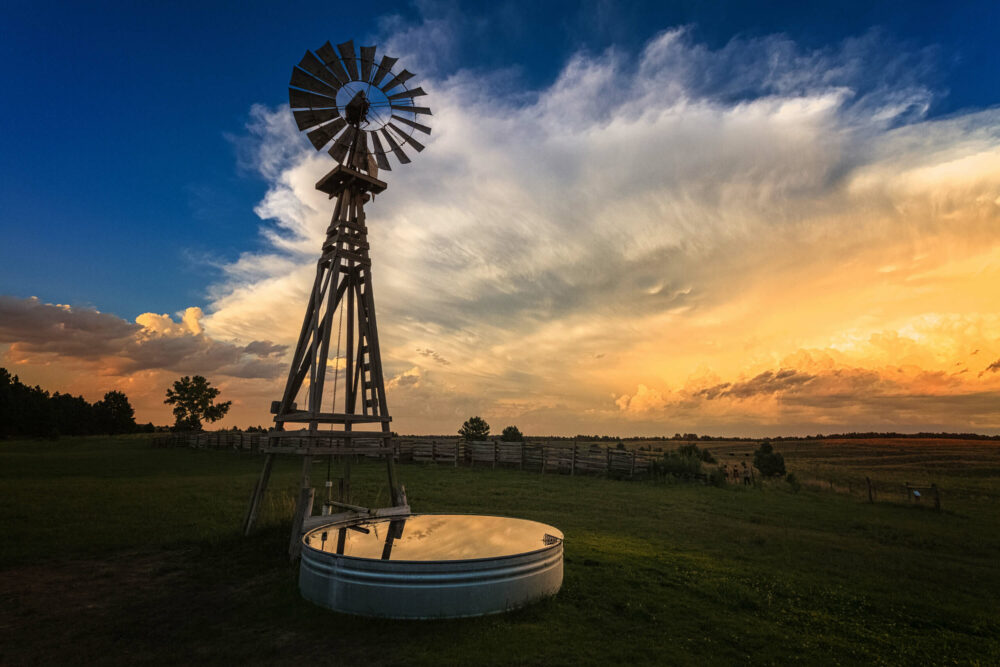 windmill in field with animal water tank reflecting blue sky