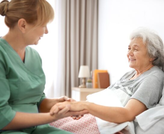 mature woman in bed offering her hand to professional female caregiver