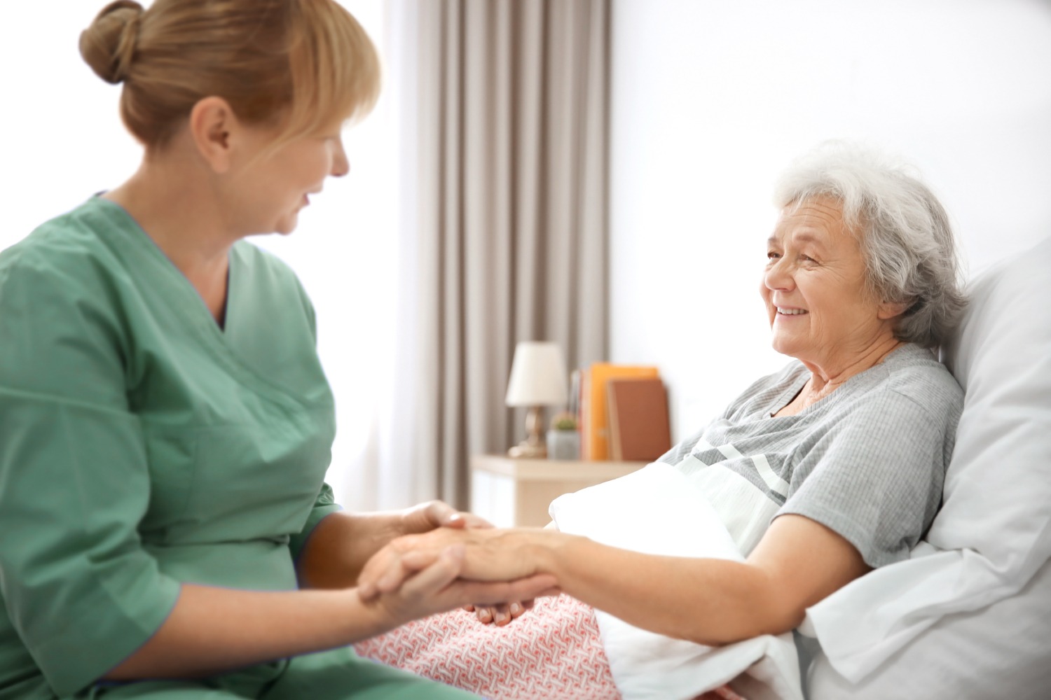 mature woman in bed offering her hand to professional female caregiver