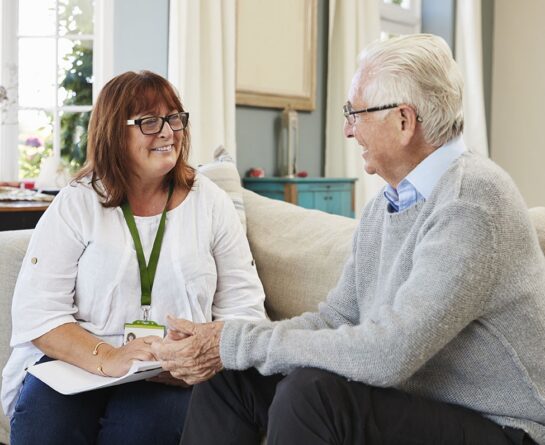 mature man and healthcare professional sitting on a sofa