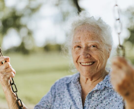 Smiling female senior sitting on a swing with blurry background