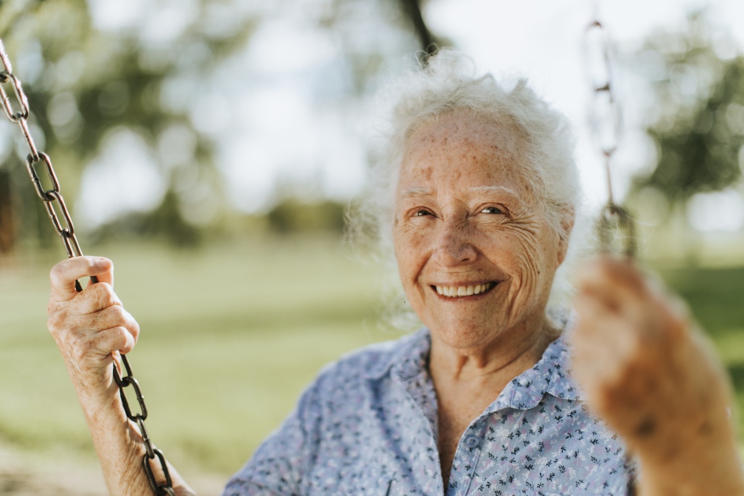 Smiling female senior sitting on a swing with blurry background