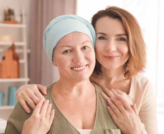 Female women smile at the camera as one of them hugs the other from the back