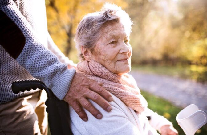 mature woman in wheelchair with mature man's hand on her shoulder