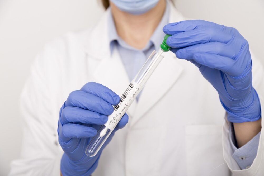 Healthcare professional wearing latex gloves holding COVID-19 testing vial and swab