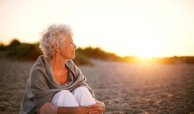 Mature woman sitting on a beach looking at a sunset