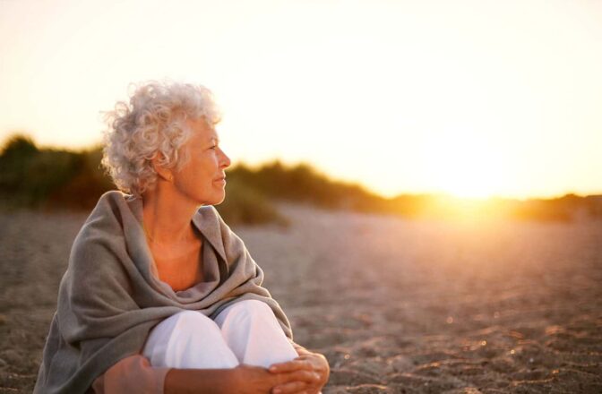 Mature woman sitting on a beach looking at a sunset