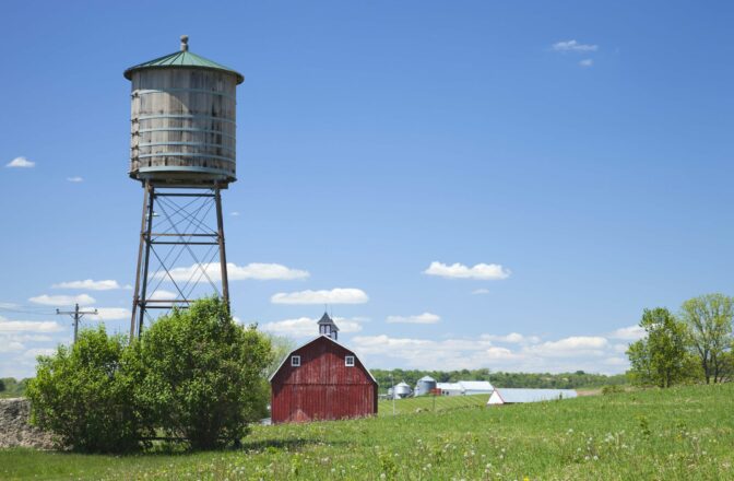early water tower in field with red barn and cupola, modern farms in distance