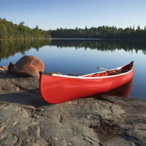 red plastic canoe resting on shore on still lake