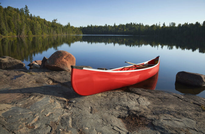 red plastic canoe resting on shore on still lake