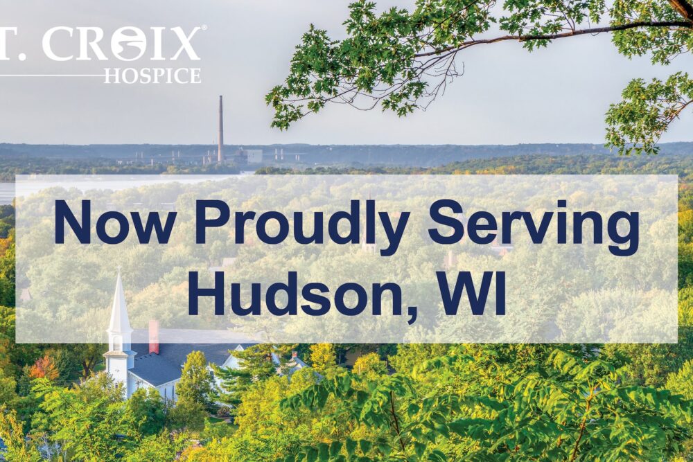 Text informing that St. Croix Hospice now serves Hudson area with green trees and city in the background