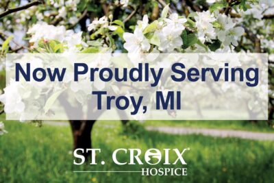 Text informing that St. Croix Hospice now serves Troy area with white flowers on tree branches in the background