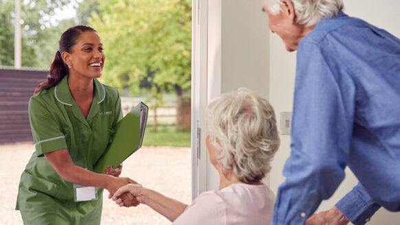 Nurse greeting senior woman in wheel chair while male senior carries her