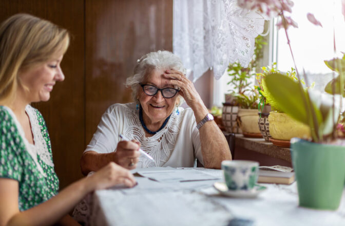 Smiling senior woman wearing glasses goes through paperwork with younger female