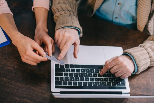 Elder's hand indicate card information as he fills it up on laptop while younger person's hand holds the card