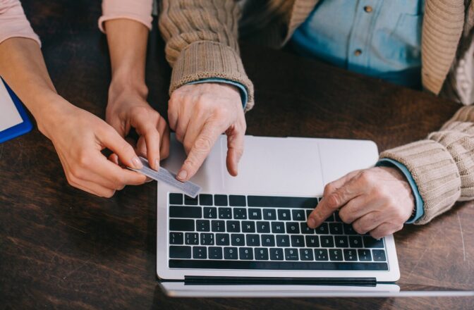 Elder's hand indicate card information as he fills it up on laptop while younger person's hand holds the card