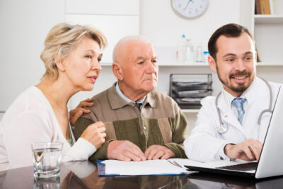 Elder couple and doctor sit on a table looking at laptop's screen