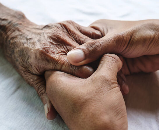 Adult's hands hold senior's hand tightly