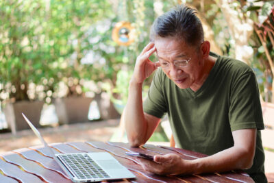 Senior man checking his phone while sitting on a table with laptop open