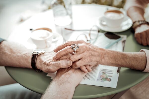 Senior couple holding hands over table with coffee cups on the back