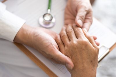 Male doctor's hands holding senior patient's hands with paperwork underneath
