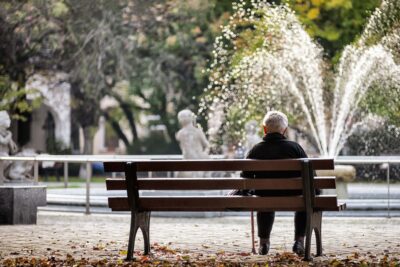 Male senior sitting alone on a bench looking at a water fountain