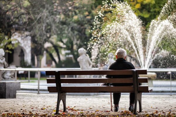 Male senior sitting alone on a bench looking at a water fountain
