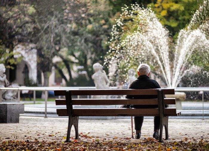 Male senior sitting alone on a bench looking at a water fountain