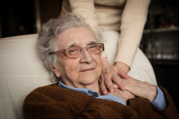 Senior woman with sad look on her face sitting on a couch holding hands with younger female