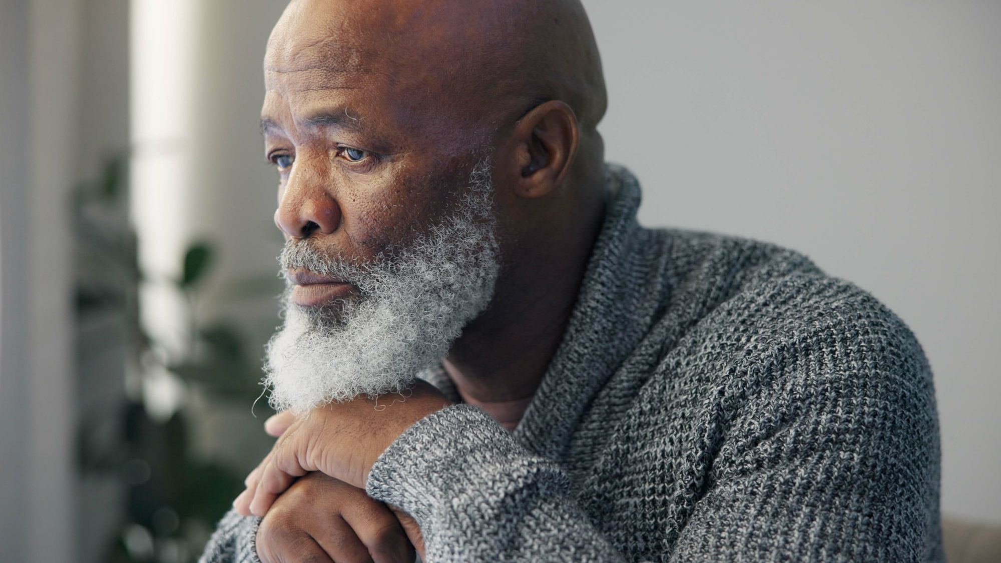 Sad senior man with beard rests chin on his hands
