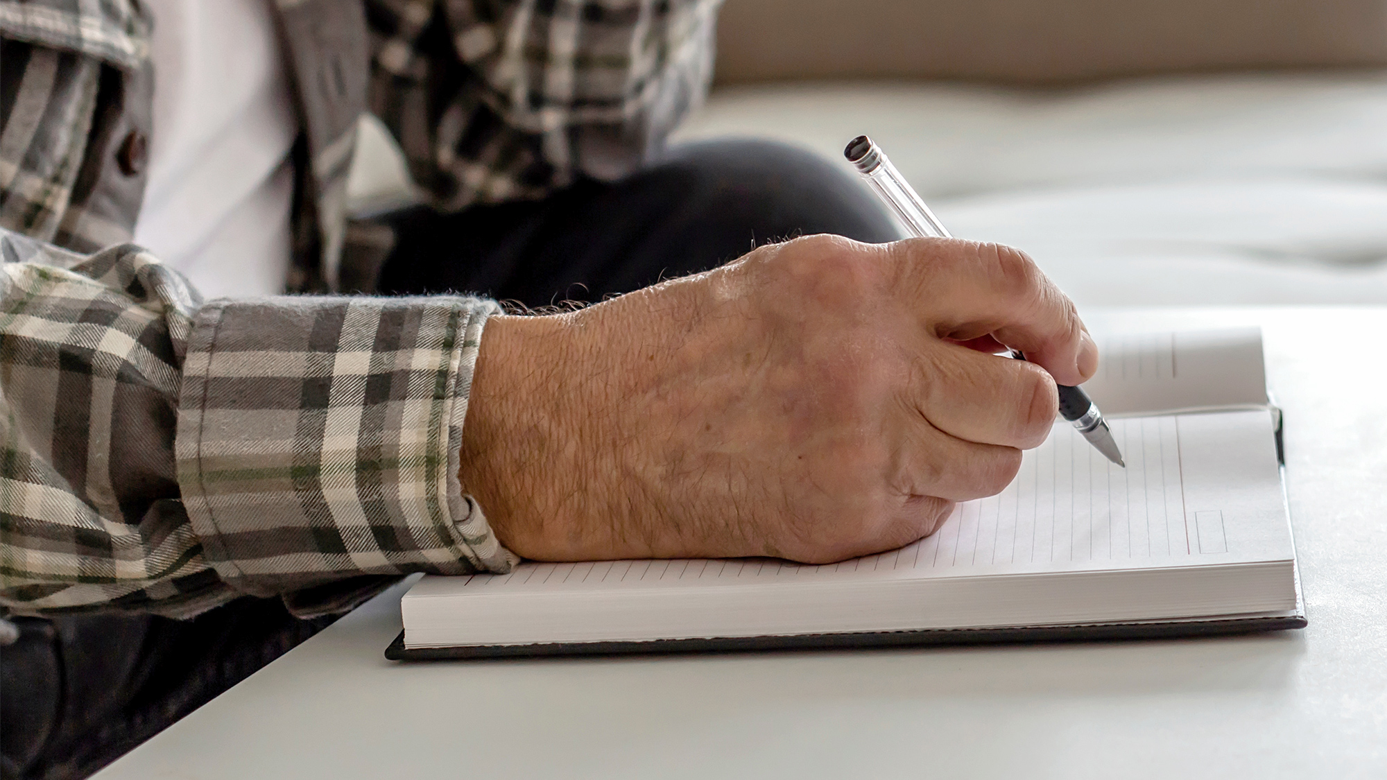 close up of person writing in a journal book wearing a flannel shirt with a pen