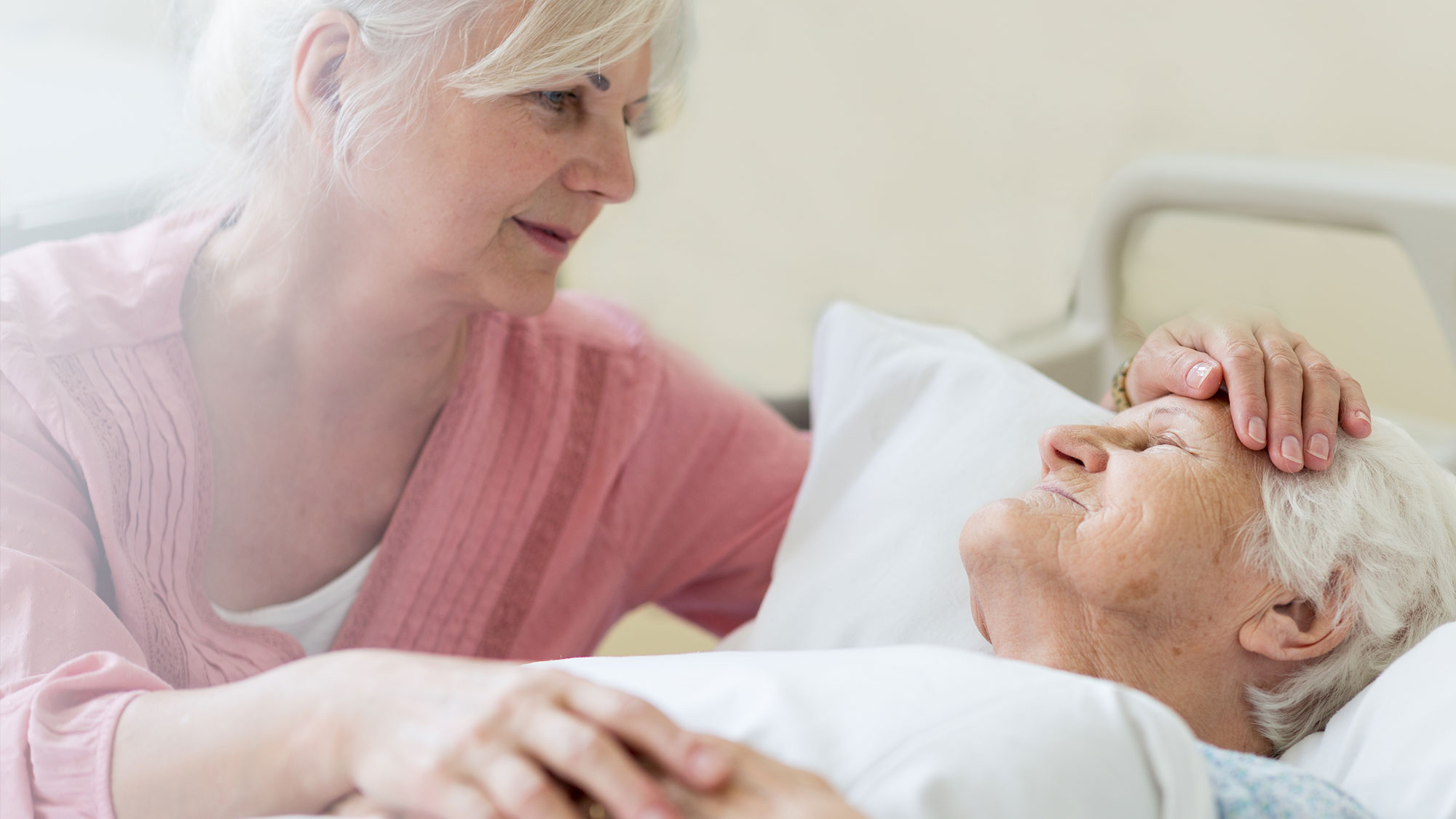caregiver comforting elderly patient in bed